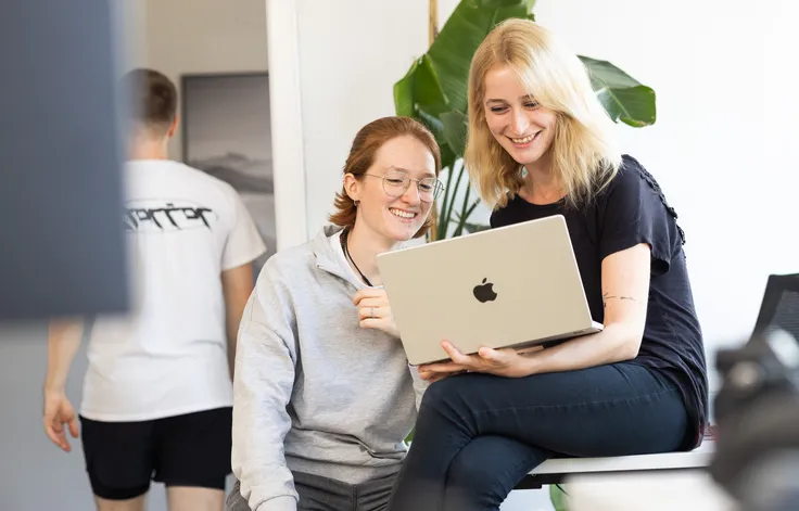 Zwei Mitarbeiterinnen, die gemeinsam auf einen Laptop schauen.